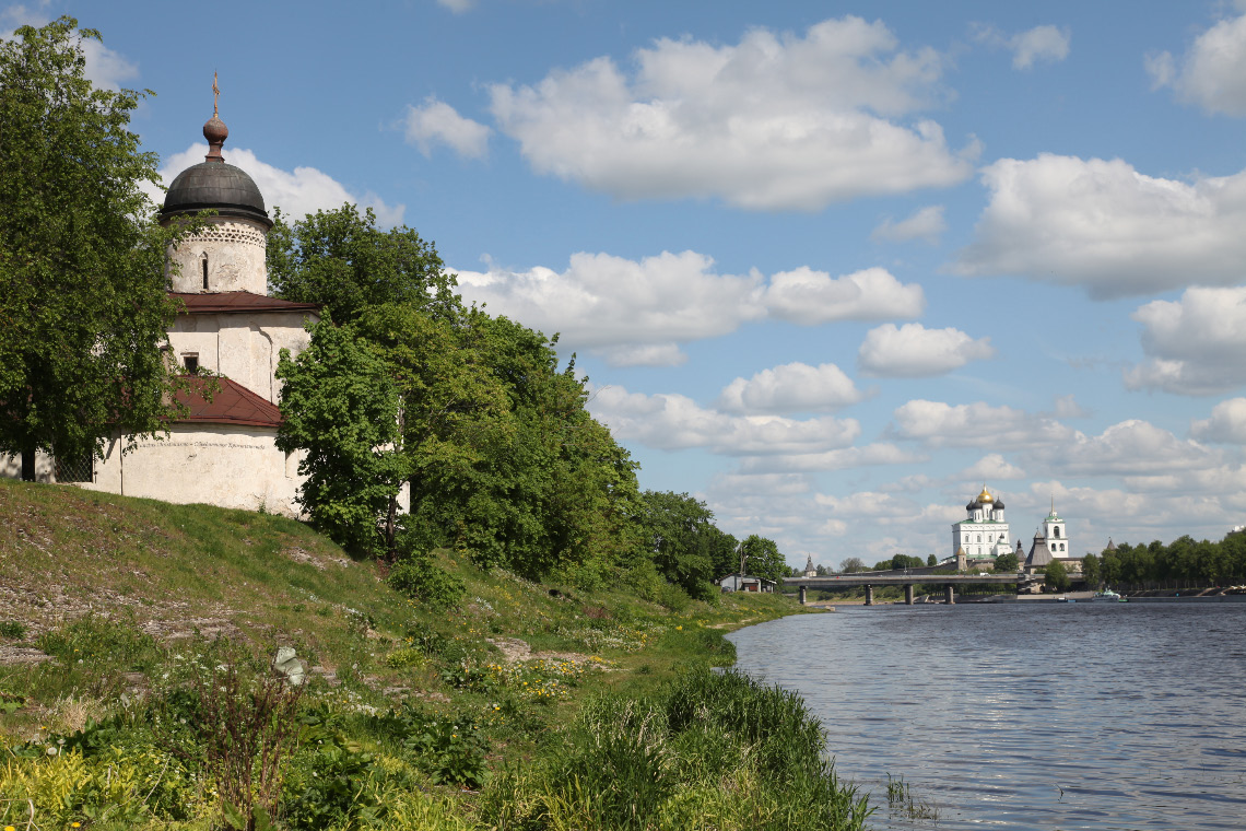 Church of Pope Saint Clement in Pskov with Krom and Trinity Cathedral in distance on opposite bank of the river